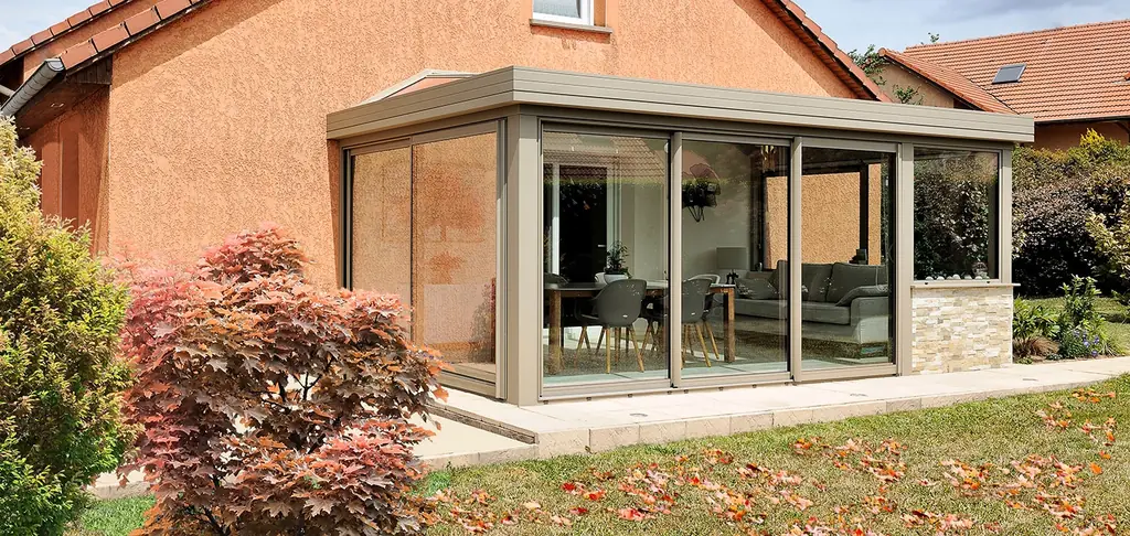 Véranda aluminium accolée à une maison aux murs ocre