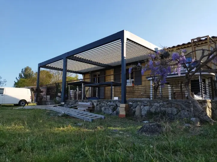 Pergola bioclimatique anthracite posée devant une maison en pierre