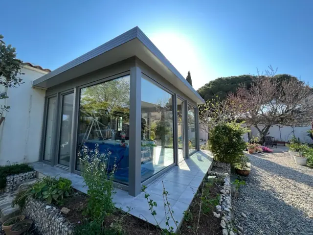 Véranda aluminium grise à toiture plate dans un jardin