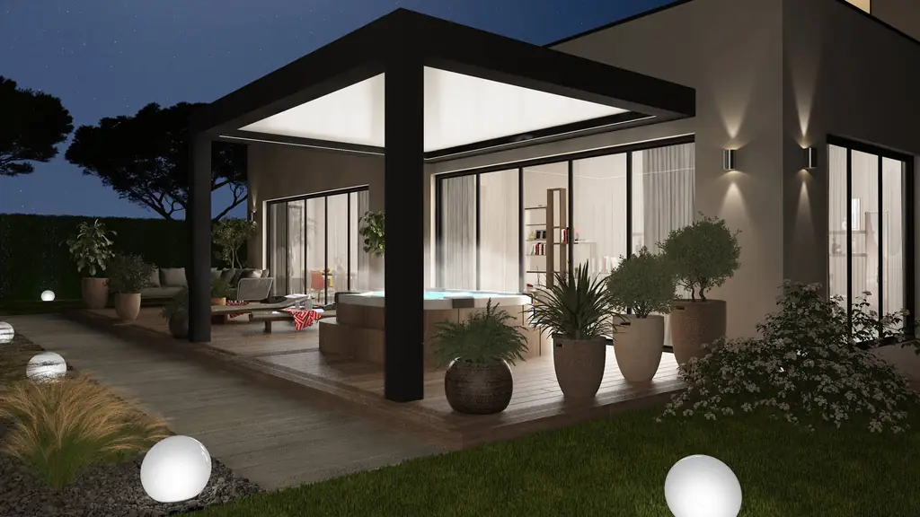 Pergola bioclimatique adossée anthracite éclairée le soir sur une terrasse